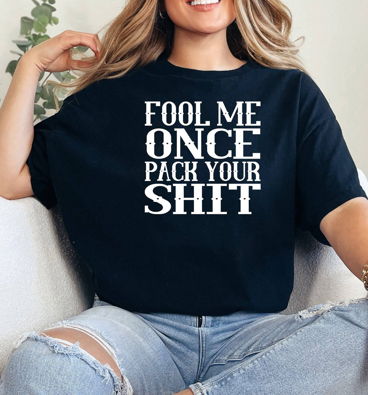 Woman wearing a black adult graphic t-shirt with white Fool Me Once Pack Your Shit lettering.