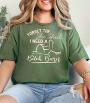 Woman wearing a military green Bitch Barn graphic T Shirt featuring a farmhouse barn design and funny She Shed saying.