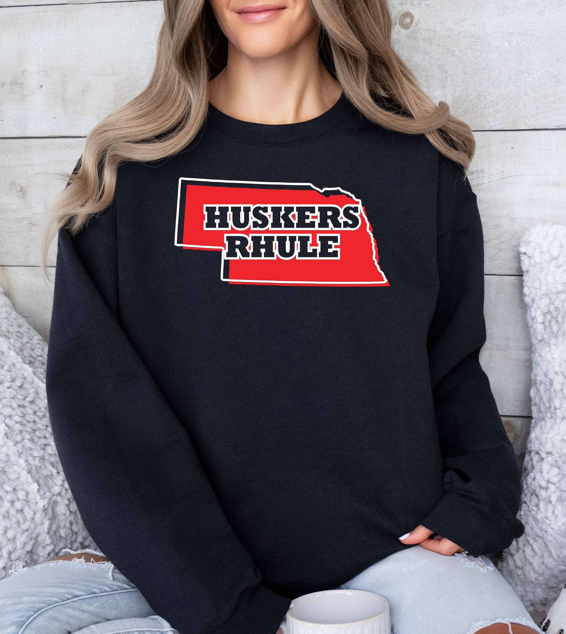 Woman wearing a black Huskers Rhule crewneck sweatshirt.