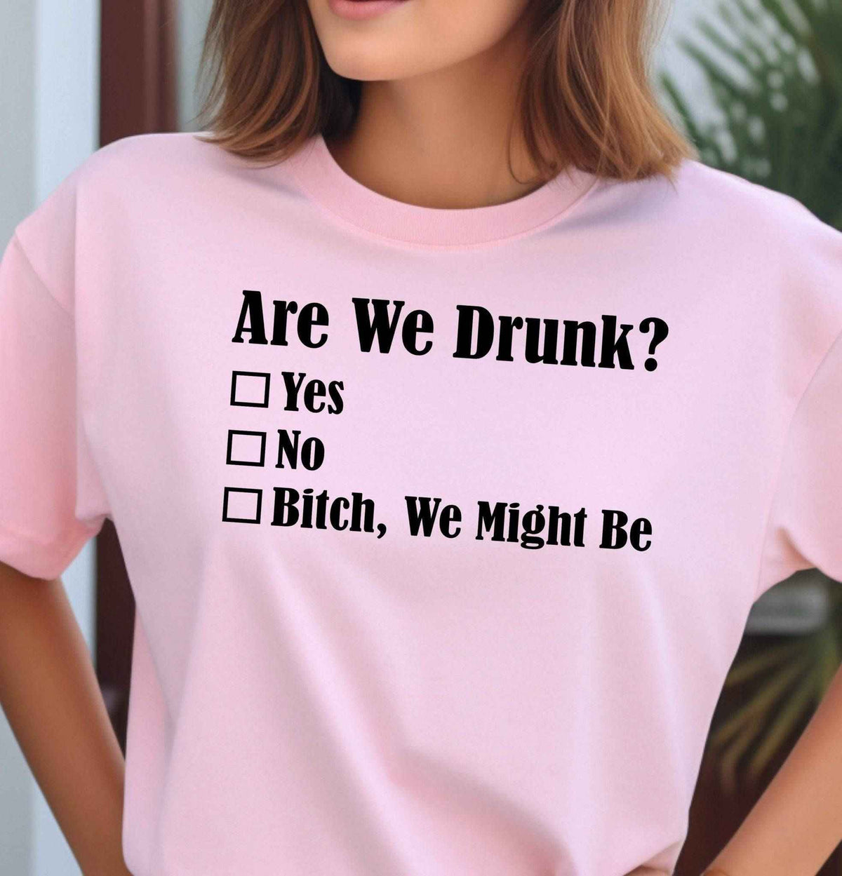 Woman wearing a pink Are We Drunk graphic T Shirt featuring a funny checklist design with the sarcastic saying Bitch, We Might Be in bold black lettering.
