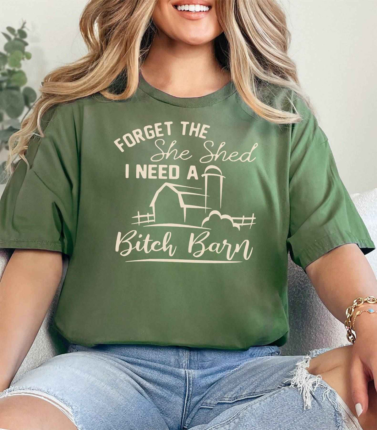 Woman wearing a military green Bitch Barn graphic T Shirt featuring a farmhouse barn design and funny She Shed saying.