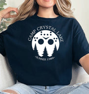 Woman wearing a black Camp Crystal Lake graphic T Shirt featuring a white hockey mask, pine trees, and Summer 1980 lettering.
