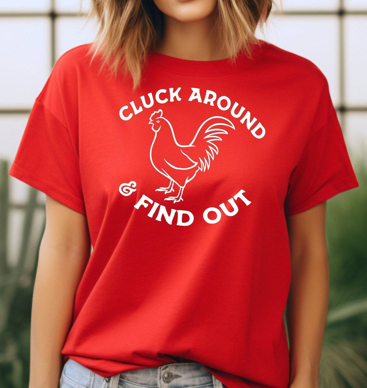 Woman wearing a red Cluck Around & Find Out graphic T Shirt featuring a white rooster illustration and bold lettering, perfect for chicken lovers and farm life fans.