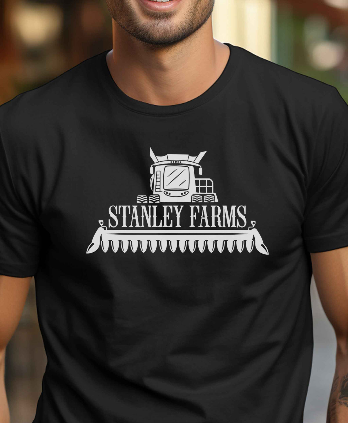 Model wearing a black custom family farm name graphic T Shirt featuring a white combine harvester design and personalized Stanley Farms lettering.