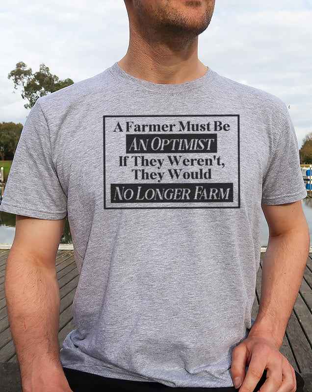 Man wearing a Sport Grey graphic T Shirt featuring the inspirational farming quote A Farmer Must Be an Optimist in bold black lettering.